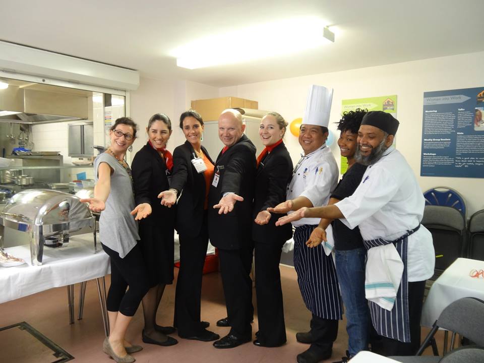 Team of employee volunteers lined up smiling at the camera, arms outstretched to form an arc.